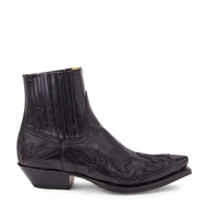 Uno stivaletto western in pelle nera di grande impatto visivo firmato Sendra, caratterizzato da una punta affusolata di grande effetto e da un tacco cubano angolato. Lo stivaletto presenta una finitura lucida e oliata con elaborati ricami in tono e inserti cuciti a forma di fiamma che attraversano la punta, la tomaia e il contrafforte posteriore. In prossimità del collo è presente un elastico laterale, mentre la suola robusta è fissata con la tradizionale cucitura Goodyear a doppia fila.