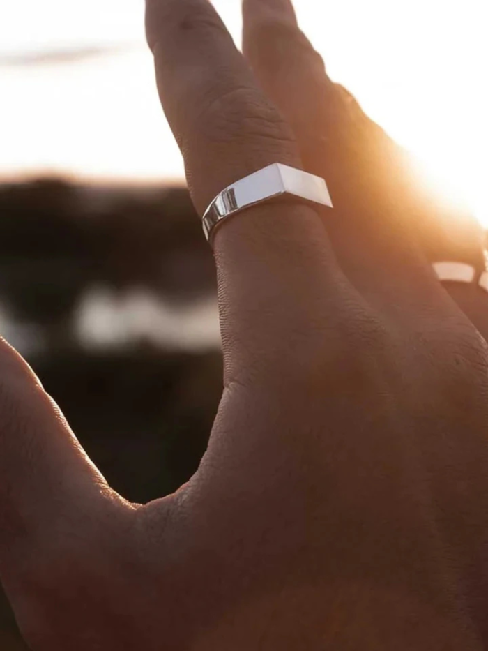 Anello argento con sommità rettangolare indossato sul dito, controluce al tramonto