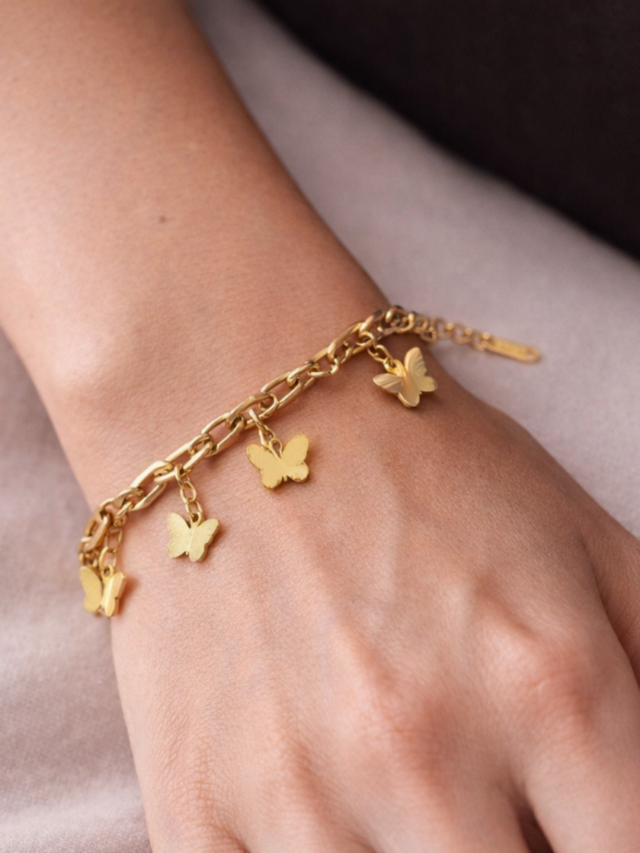Bracciale dorato con charms a forma di farfalla indossato al polso