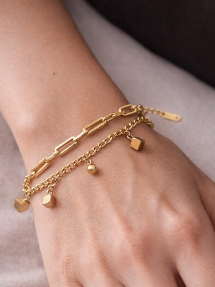 Bracciale dorato a doppia catena con piccoli cubi e sfere indossato al polso