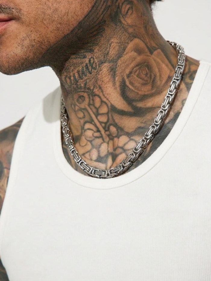 Collana a maglia bizantina color acciaio indossata su canotta bianca da un ragazzo con tatuaggi sul collo