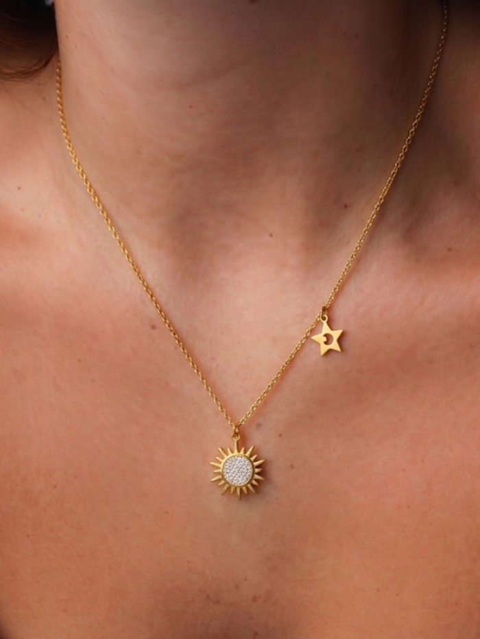 Collana dorata con pendente a sole e piccola stella laterale indossata sul décolleté