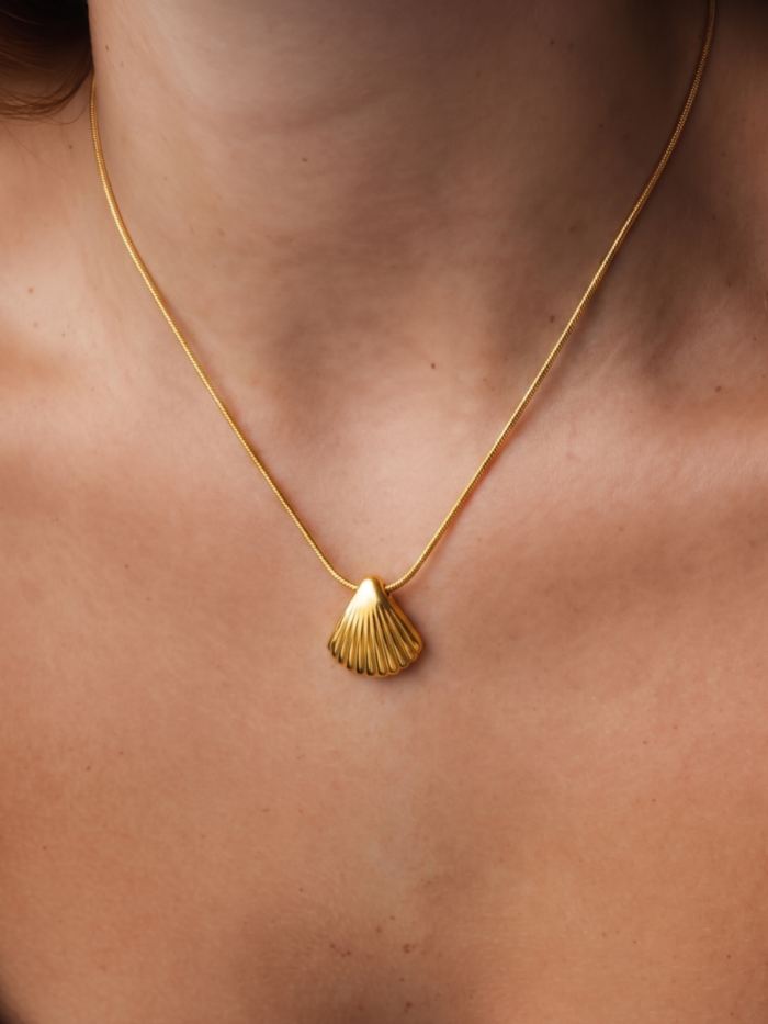 Collana dorata con pendente a conchiglia indossata sul décolleté
