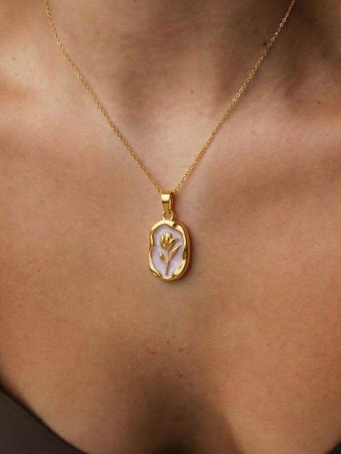 Collana dorata con medaglione ovale e fiore in rilievo indossata sul décolleté
