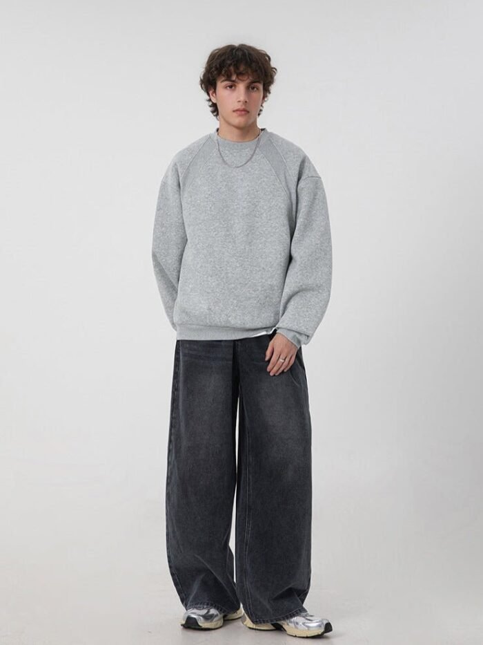 Modello a figura intera con felpa grigia girocollo, jeans ampi in denim scuro e sneakers