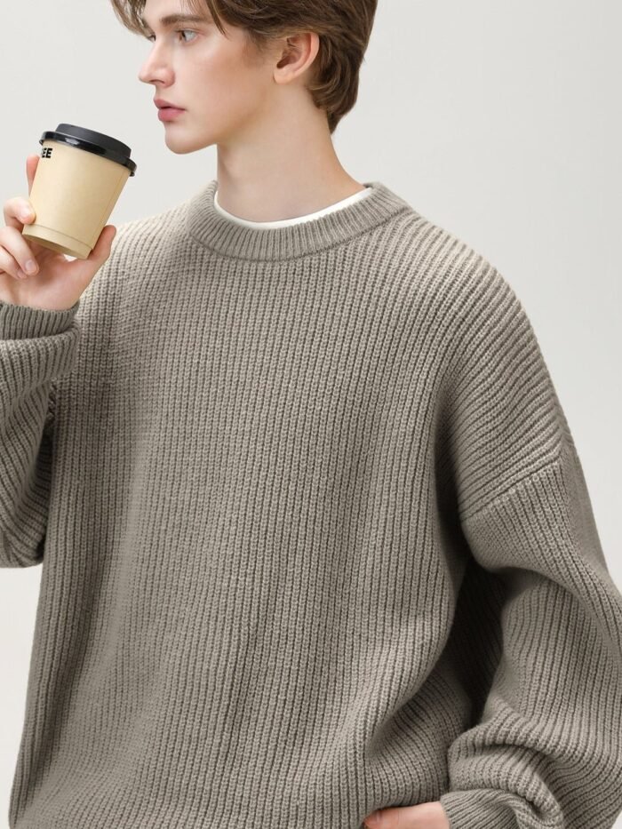 Maglione grigio a coste con spalle scese, primo piano del modello con tazza di caffè