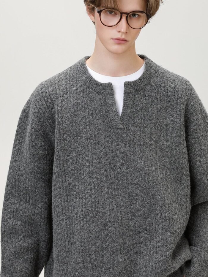 Dettaglio della maglia texturizzata e dello scollo a spacco del maglione grigio, modello con occhiali