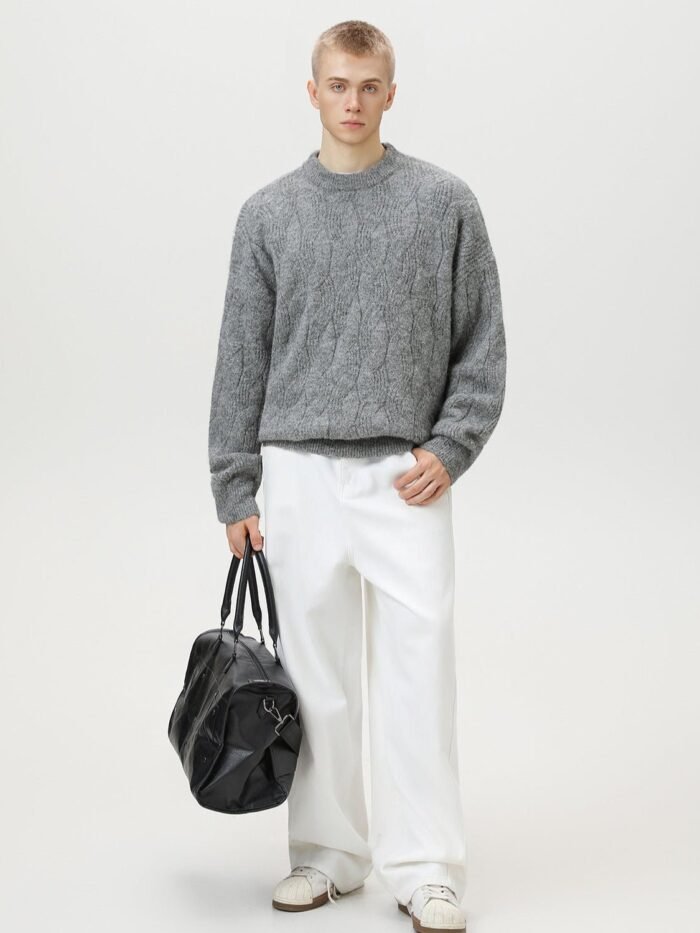 Modello a figura intera con maglione a trecce grigio, pantaloni bianchi ampi, sneakers e borsa nera in pelle