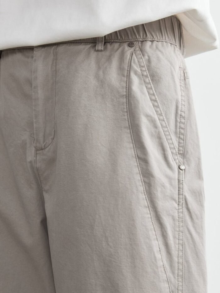Dettaglio della tasca laterale obliqua con impunture e rivetti e dell’elastico in vita sui pantaloni grigi