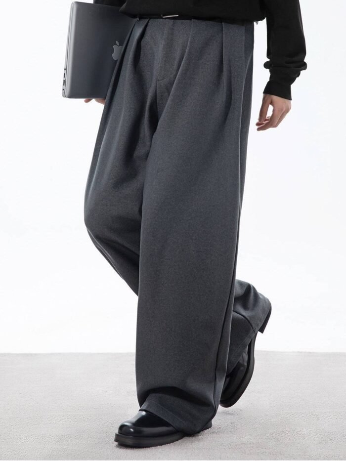 Pantaloni grigi con pieghe frontali visti di lato mentre il modello cammina con scarpe in pelle nera