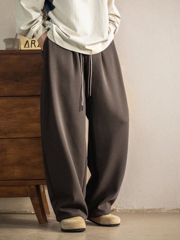 Pantaloni a gamba ampia marroni con coulisse in vita visti di tre quarti, accanto a una cassettiera in legno